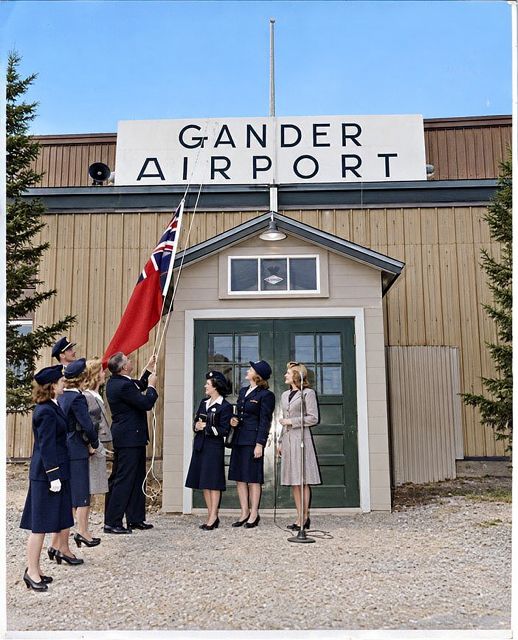 Uniformed women and officials raising a flag in front of the Gander Airport building