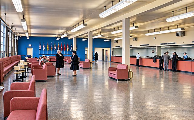 The wide terminal lounge with pink armchairs, a blue wall and airline counters along the right side